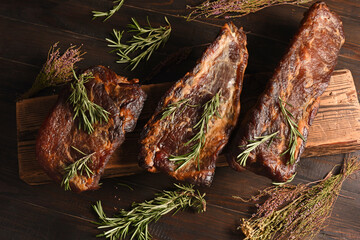 Dried Processed Beef Jerky with herbs and spices on wooden board against black background.