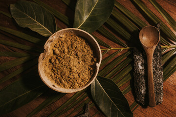 Yellow powder in organic recipient with wooden spoon on top of green leaves from the tropical jungle 