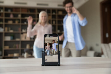Fototapeta na wymiar Close up of smartphone screen recording video of young adult son and senior mother posing in home living room, dancing, waving greeting hands hello, standing, smiling, laughing, having fun