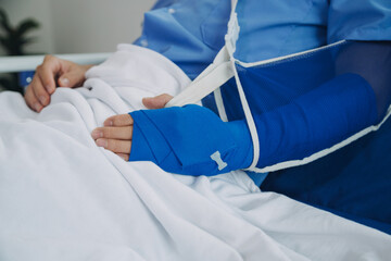 Man with broken arm in cast lying on bed in hospital. The emergency center treatment is plaster and...
