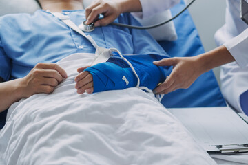 Man with broken arm in cast lying on bed in hospital. The emergency center treatment is plaster and hangs with sling for a further cure in an orthopedic clinic. Patient pain from accident injury.