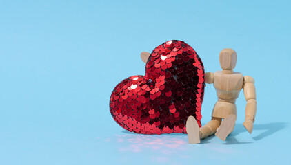 Wooden mannequin and red heart made of sequins on a blue background