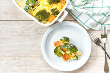 Casserole broccoli with cheese and cream sauce in a bowl on a white wooden table, top view.