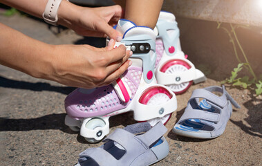 Close-up Mother putting on inline skates rollers to daughter child in public park in summer. Family...