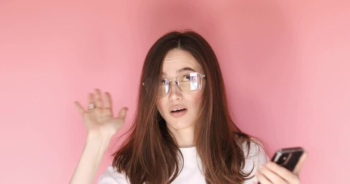 Exhausted tired young woman look at mobile phone showing mind explosion gesture, feeling unhappy and nervous, lots unnecessary information isolated on pink background. 