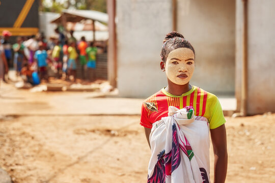Unrecognizable Malagasy girl with white clay mask on her face, dressed in colorful native clothing. Semi-portrait, real life in rural Madagascar. 