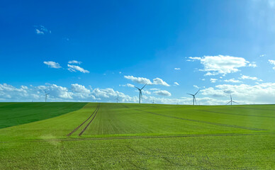 Windmills on the background of a green field and a blue cloudy sky. Wind turbine for power generation