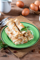 Thin pancakes with cottage cheese and raisins on wooden table. Healthy traditional breakfast concept.
