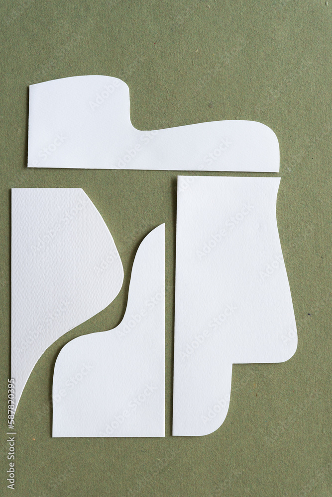 Wall mural cut white paper shapes with distinct wavy and straight edge forms on rough green paper