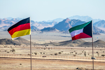 German and Kuwaiti flags waving togetner on the wind in Saudi Arabian desertwith mountains in background, Al Ula, Saudi Arabia