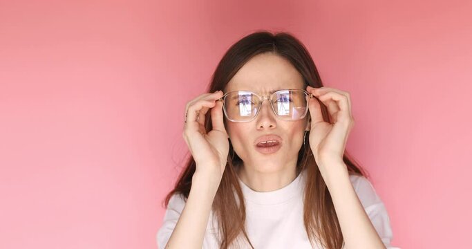 Girl with poor vision looking at camera and rejoicing after putting on eyeglasses isolated against pink background. Young brunette woman with vision problems seeing perfectly with eyeglasses. Try see.