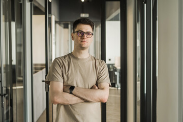 Portrait of a serious millennial male business owner in modern office. Businessman wearing glasses, looking out window. Leadership concept. Head shot