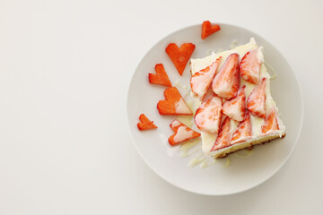Piece of homemade pie with whipped cream and strawberries heart shape red berries on white plate on white table postcard copy space valentines day homemade bakery