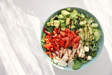 Fresh green salad on round green table white floor sunny day sunshine pepper, cucumber, avocado, balsamic souse copy space horizontal vegan food plate