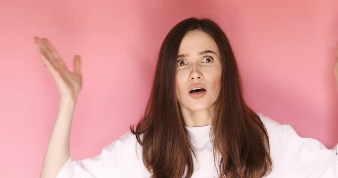  A displeased young woman spread hands, ask what and rolls her eyes isolated over pink background. Caucasian lady in displeasure, she is tired of situation, thinks how cant you still not understand.