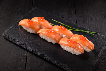 Sushi with salmon and red caviar on a black stone board on a dark background.