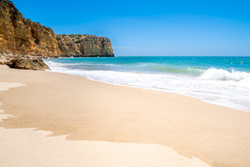 Praia do Canavial, a hidden gem of an Algarve beach, features pristine sand, sparkling blue waters and a gentle wave breaking against the rocky cliffs, providing an idyllic scene devoid of any crowds.