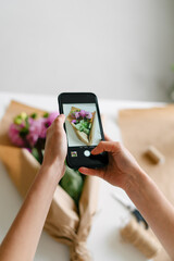 A woman takes a photo of a bouquet of dahlias on the phone, vertical image
