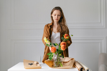 A young woman in a brown shirt, a florist, collects a bouquet of orange dahlias in a vase. An authentic portrayal of a small business