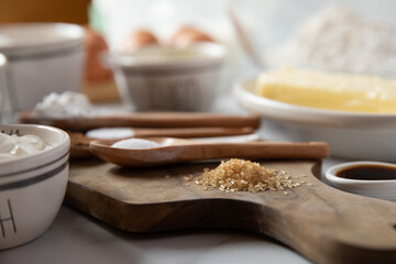 Baking ingredients in measuring spoons and bowls sit on a white marble surface and wooden cutting board.