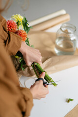 Vertical image of a female florist cutting dahlia flowers before packing them into a bouquet. Image for your design