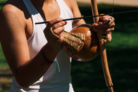 vista de manos de mujer capoeira tocando instrumento berimbau con vista desde cerca en un d&iacute;a soleado en un parque.