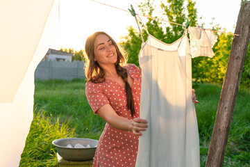 Young woman hanging laundry outdoors. Beautiful girl in red polkadot dress. working in countryside....