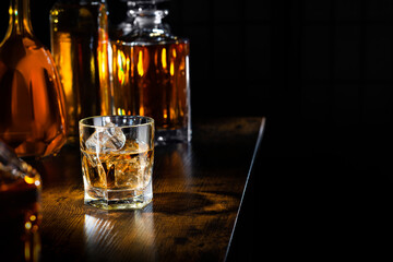 Whisky Glas mit Eiswürfeln und Flaschen mit Whisky auf einem Tresen