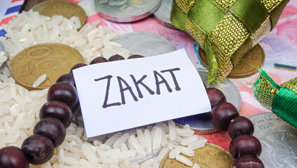 Phrase ZAKAT written on white tag with rice, rosary beads (tasbih) and coins. Selective focus