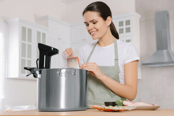 Woman putting vacuum packed salmon into pot with sous vide cooker in kitchen. Thermal immersion...