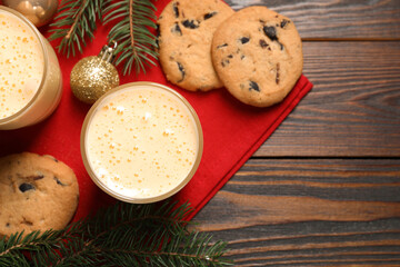 Tasty eggnog, cookies, baubles and fir branches on wooden table, flat lay. Space for text
