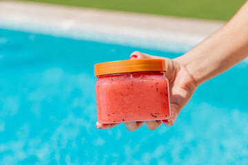 Mano femenina sosteniendo un pote frasco de crema con piscina en fondo aislado. Vista de frente....