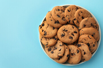 Bowl of delicious chocolate chip cookies on light blue background, top view. Space for text