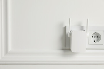 Wireless Wi-Fi repeater on white wall indoors, space for text