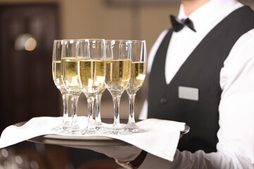 Butler holding tray with glasses of sparkling wine in restaurant, closeup