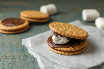 Delicious marshmallow sandwich with crackers and chocolate on light blue wooden table, closeup. Space for text