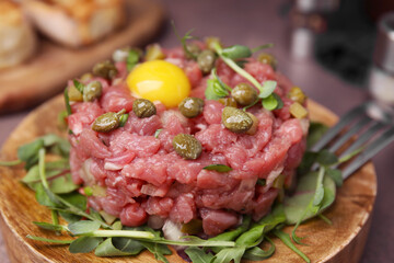 Tasty beef steak tartare served yolk, capers and microgreens on serving board, closeup
