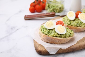 Delicious sandwiches with guacamole, eggs and tomatoes on white marble table, space for text