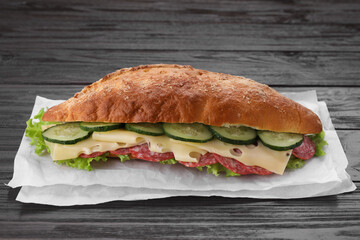 Delicious sandwich with cucumber, cheese, salami and lettuce leaves on wooden table