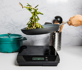 A pan of asparagus being tossed over a stove