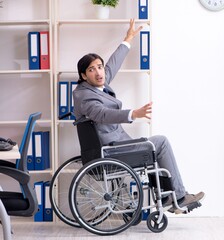 Young handsome employee in wheelchair working in the office