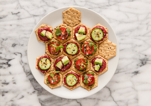 Appetizers of crackers with veggies, pesto, avocado and herbs