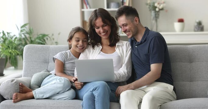 Happy Hispanic couple and little cute daughter resting together on couch watch funny videos, movie on-line, spend pastime on internet use laptop. Family leisure at home with modern wireless technology