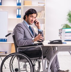 Young handsome employee in wheelchair at the office