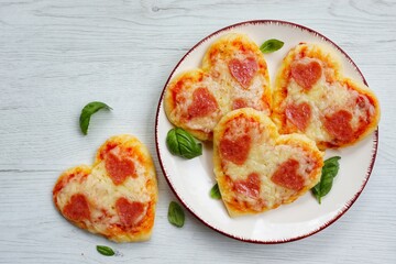 Heart shaped mini pizzas with heart shaped pepperoni on plate with white wood background.Creative art food idea for celebrate Valentine or Mother day.Top view.Copy space

