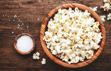 Salted popcorn in wooden bowl, unhealthy food, wooden kitchen table background, top view