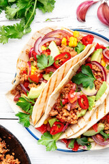 Tacos with beef, corn, red beans, tomato salsa sauce and red onions in corn tortilla on plate. Mexican cuisine. White table background, top view