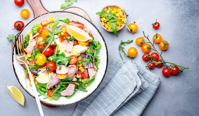 Canned tuna salad with cherry tomatoes, red onion, eggs, sweet corn, paprika, lettuce, radicchio and arugula. Gray table background, top view