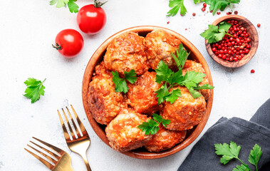 Pork and beef meatballs in tomato sauce in wooden bowl on white table background, spices and herbs. Delicious home cooking. Top view