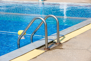 Fototapeta na wymiar Ladder stainless handrails for descent into swimming pool. Swimming pool with handrail . Ladder of a swimming pool. Horizontal shot. stairs swimming pool. Stainless steel ladder